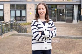 Gemma Donegan standing outside a healthcare building. Gemma is standing with her arms folded. She is wearing a black and white striped cardigan.